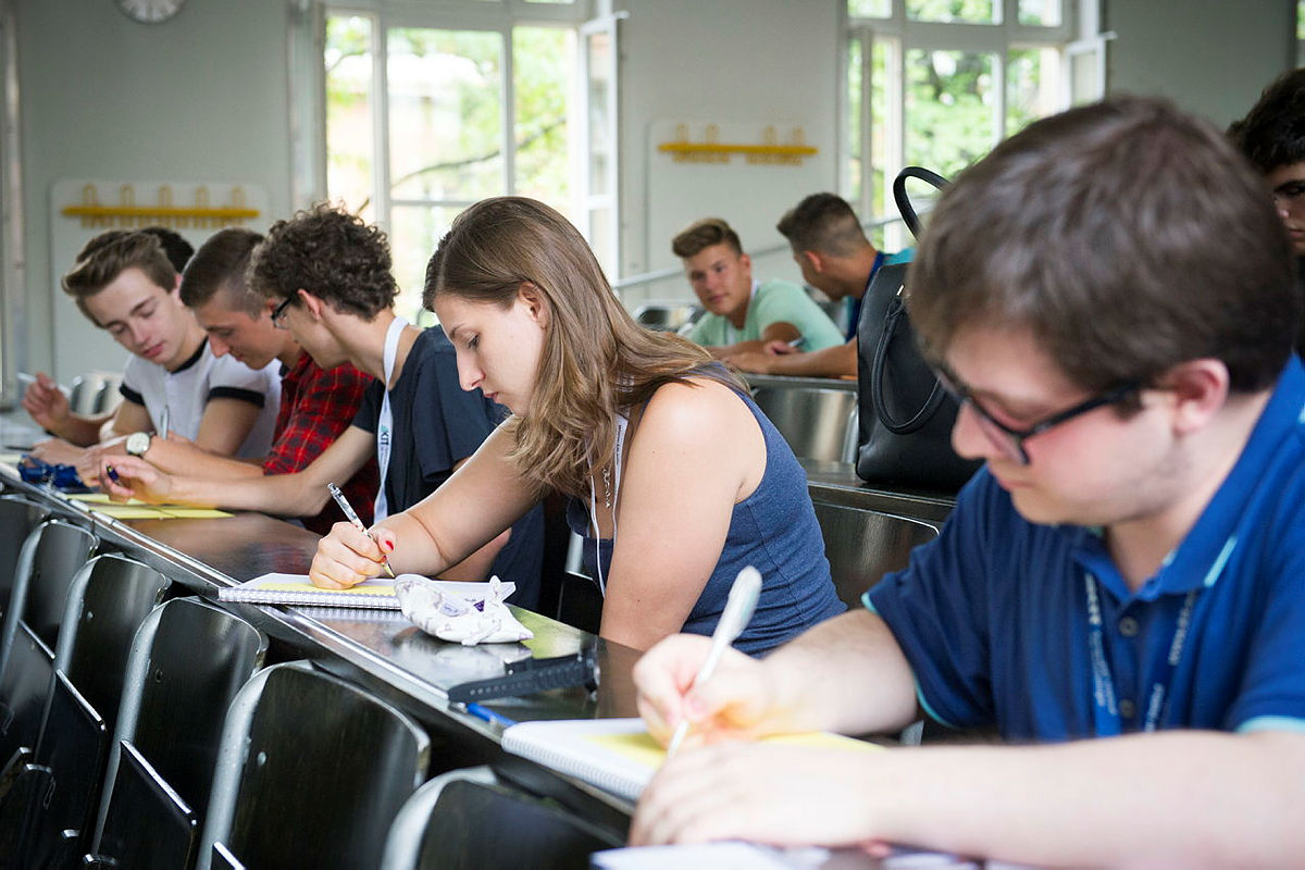 Eine Grupp von Studierenden sitzt in einem Hörsaal und schreibt in ihre Unterlagen