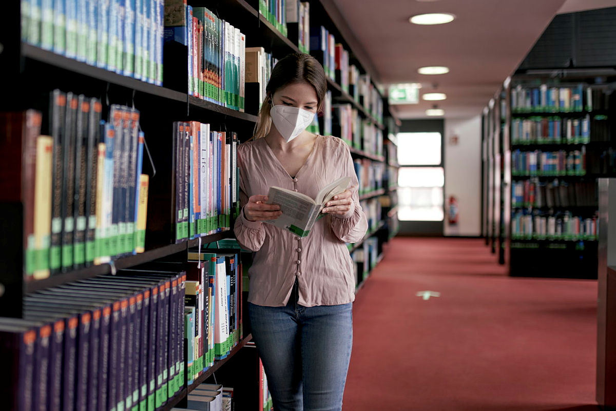 Eine Geisteswissenschaftlerin steht in der Bibliothek an ein Regal gelehnt