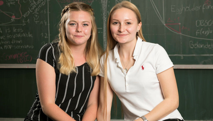 Zwei Studentinnen sitzen nebeneinander auf dem Tisch in einem Hörsaal