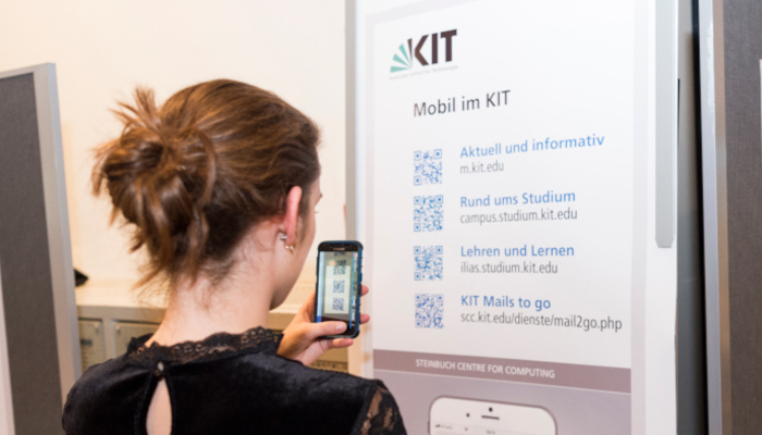 Junge Frau scannt mit dem Smartphone Informationen zu den Diensten für mobile Geräte vom Info-Plakat